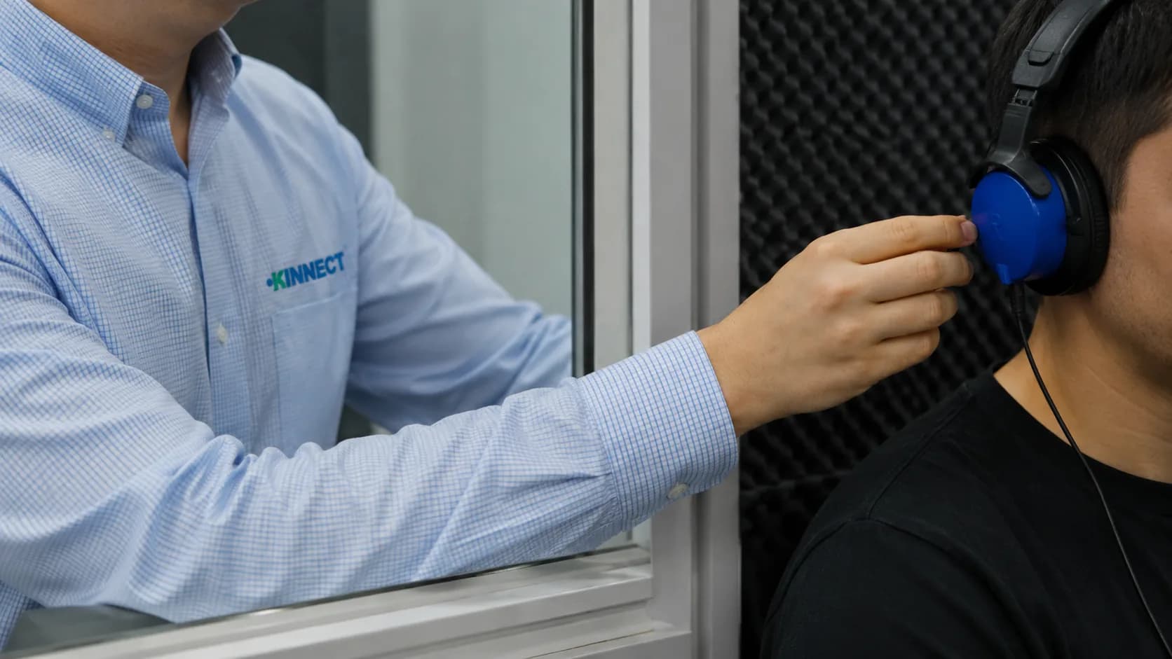KINNECT clinician fitting headphones for a worker's audiometry test inside a sound-attenuating booth