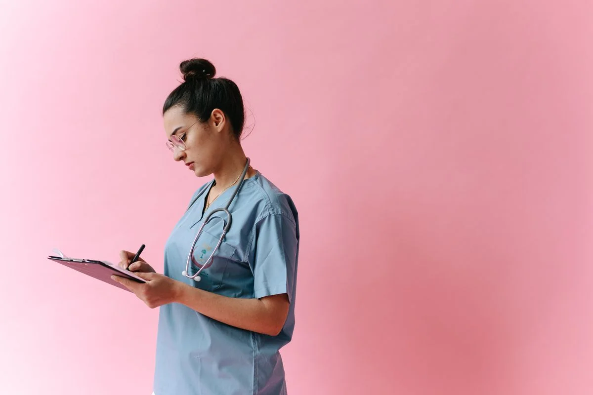 Healthcare professional in blue scrubs writing notes on a clipboard — illustrative stock photograph