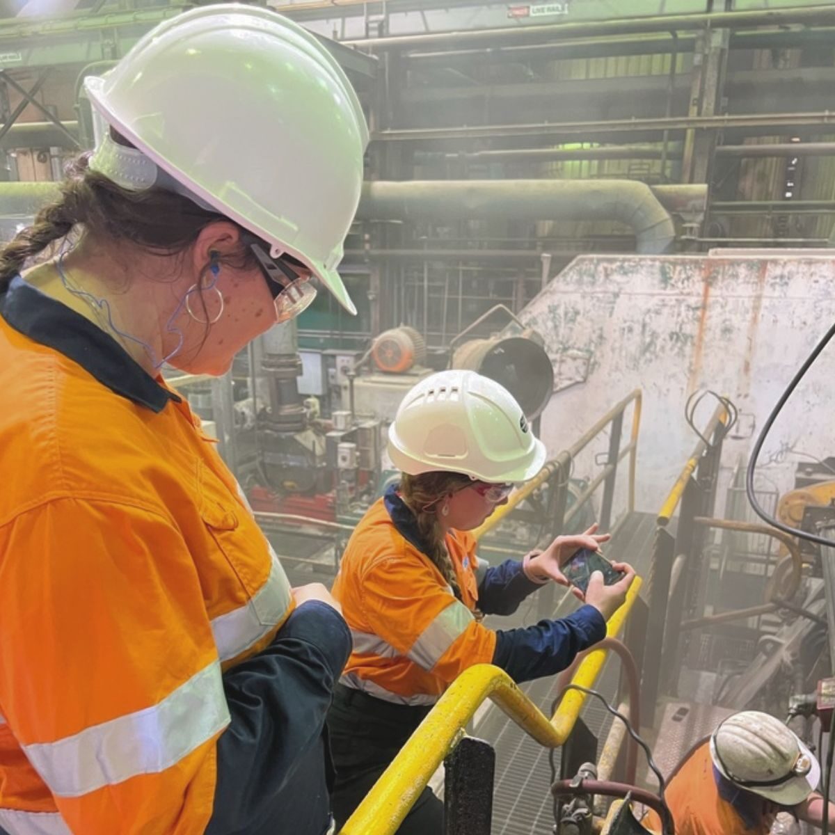Two KINNECT clinicians in hi-vis and hard hats reviewing data on a phone at a heavy-industrial site