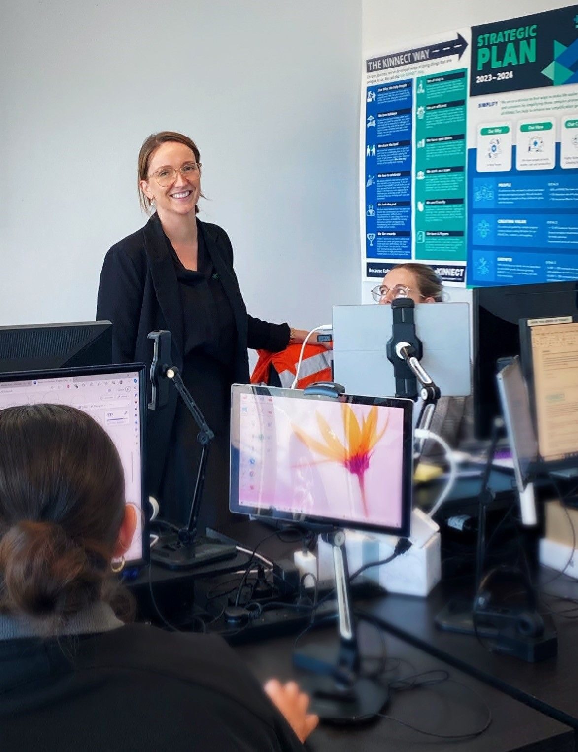 A KINNECT team member smiling at a desk in front of The KINNECT Way and Strategic Plan posters